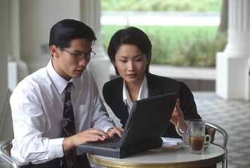 Male and female executives working on laptop computer in cafe