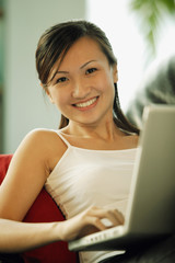 Young woman on sofa, using laptop, looking at camera