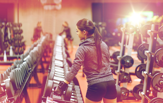 young woman choosing dumbbells in gym