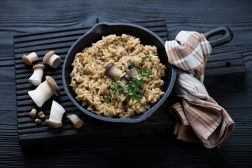 Risotto with ceps in a frying pan over black wooden background