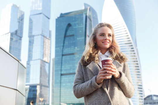 Beautiful young woman holding coffee on background of skyscrapers