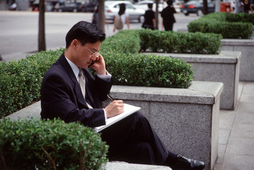 Obraz premium Man in business suit, using mobile phone and writing on note pad