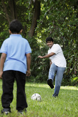 Father kicking ball to son