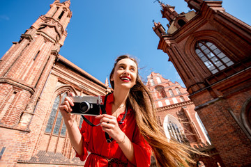 Young female tourist with photo camera standing in front of the famous gothic church in the old town of Vilnius. Woman having great vacations in Lithuania