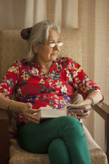 India, Senior woman sitting in armchair reading book