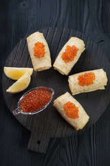 Rolled crepes with salmon caviar over black wooden surface