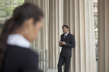 India, Businessman using mobile phone looking up at colleague in distance