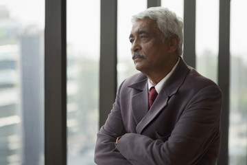 India, Portrait of senior businessman with arms folded looking through window