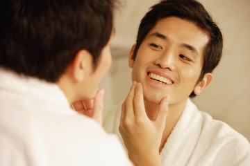 Young man touching his face, looking in mirror