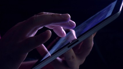 Hand gestures over tablet computer in dark room. Purple glowing touchscreen