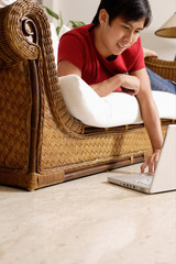 Man lying on sofa, using laptop resting on floor