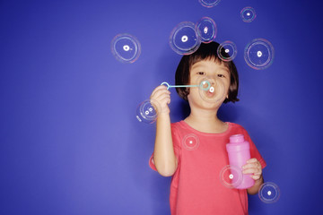 Young girl with bubble wand, blowing bubbles