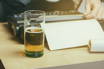 Escritor con su máquina de escribir y un folio en blanco que tiene una cerveza sobre su mesa 