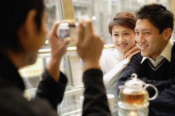 Couple posing as their friend takes their picture