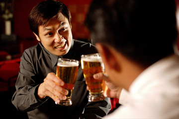 Two men toasting with beer glasses, over the shoulder view