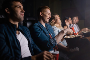 Young man with friends watching movie in cinema - obrazy, fototapety, plakaty