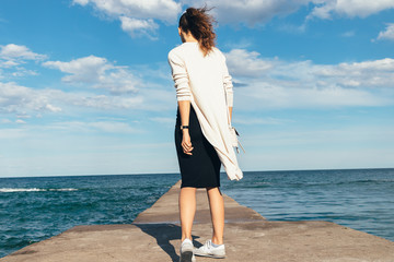 Slim brunette woman in a skirt, cardigan and sneakers walking on