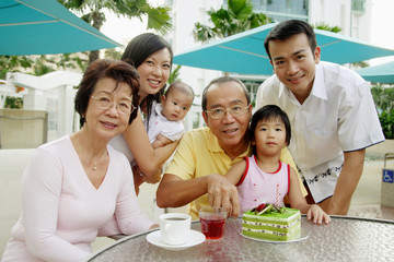 Three generation family, grandfather cutting cake, looking at camera