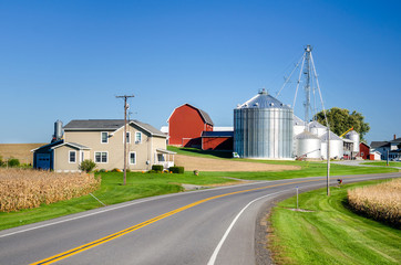 Fototapeta na wymiar Farm with Silos and Red Barn along a Country Road under Clear Sky