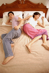 Couple lying in bed, back to back