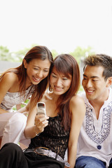 Young women and young man looking at mobile phone, smiling