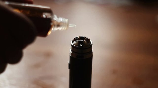 Man filling an electronic cigarette with e-juice. Man detaching the reservoir tank from the atomizer and battery to fill it with flavored liquid (e-juice) that may or may not contain nicotine.
