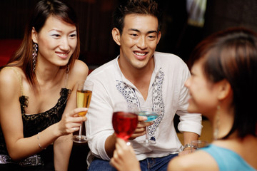 Couple holding drinks, facing another young woman