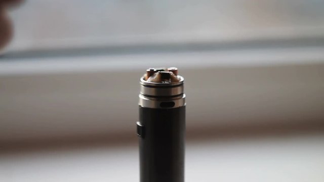 Man filling an electronic cigarette with e-juice. Man detaching the reservoir tank from the atomizer and battery to fill it with flavored liquid (e-juice) that may or may not contain nicotine.