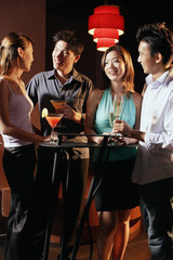 Young adults in night club, standing and holding drinks