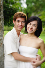 Fototapeta premium Couple leaning on tree, embracing, looking at camera