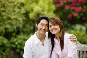 Couple sitting on park bench, smiling at camera