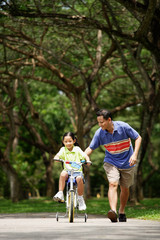 Girl cycling, father running next to her