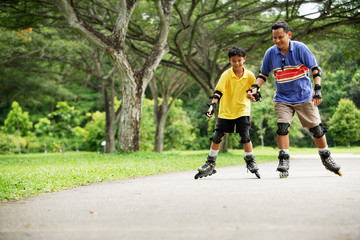 Father and son, in-line skating in park, holding hands