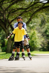 Father and son, in-line skating in park, father holding son from behind