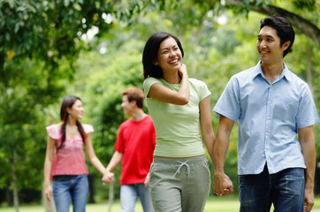 Couple holding hands and walking in park, people in the background