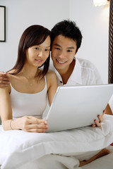 Couple sitting on bed, using laptop