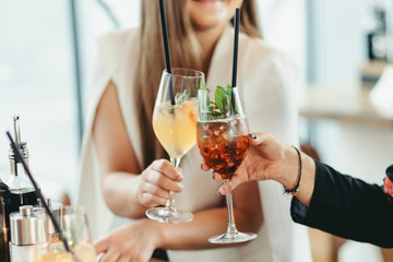 hands of two unknown women holding cocktails in restaurant
