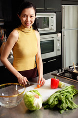 Woman in kitchen, cutting vegetables, smiling at camera