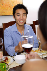 Man at dinner table, holding wine glasses, facing another person