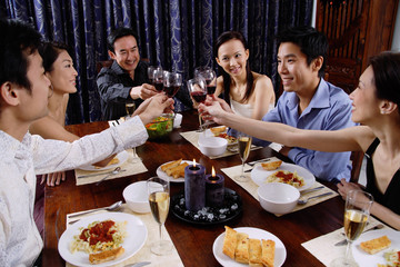 Adults at a dinner party, sitting around table, toasting