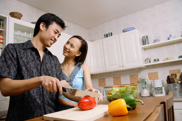 Couple in kitchen, man cutting vegetables, woman smiling at him