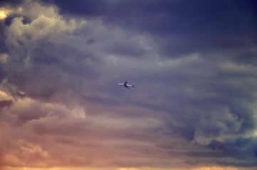 The airplane passenger jet fly right in to the dark clouds just before storm. Colorful sunset rays. Emergency concept.