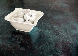 
Almonds coated with chocolate and icing sugar in small white porcelain bowl isolated on black marbled background. Selective Focus and lots of copy space.