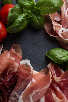 Ham mix. Jamon. Traditional Italian and Spanish salting, smoking, dry-cured dish - jambon Serrano and prosciutto crudo sliced with herbs and tomatoes on dark stone background. Copy space. Closeup. 