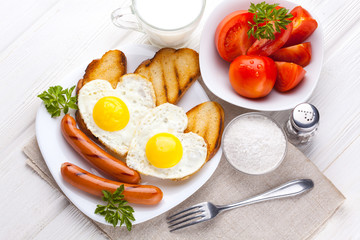 Breakfast on Valentine's Day - fried eggs in the shape of a heart and sausages. Top view