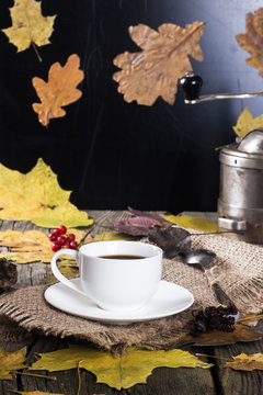 white cup of coffee on a background coffee grinder on the old wooden board with yellow leaves