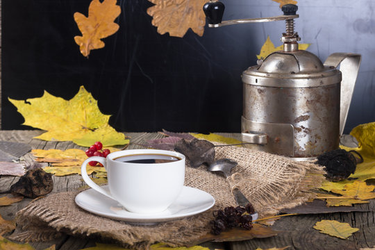 white cup of coffee on a background coffee grinder on the old wooden board with yellow leaves