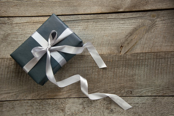 Gift box wrapped in black paper with silver ribbon on wooden surface.