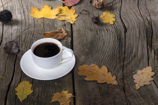 white cup of coffee on a wooden background with autumn leaves