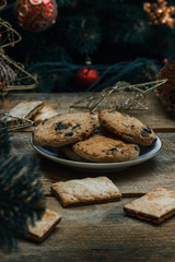 Beautiful concept. Chocolate cookies on a white plate on a wooden background. Nearby stands a Christmas tree, toys, garlands and Christmas toys.